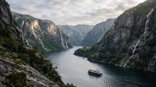 A small fjord cruise vessel navigating between towering cliffs on a Norwegian fjord at golden hour