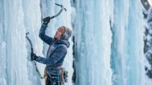 A climber swinging an ice tool into a frozen waterfall, focused and determined, surrounded by blue ice formations