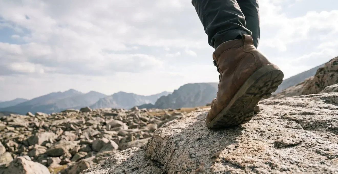 Hiker carefully placing a trekking boot on a jagged rocky ridge during a mountain trek