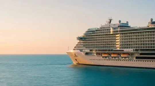Wide editorial photograph of a massive modern cruise ship resembling a floating resort hotel at golden hour, symbolizing the comparison between ocean liners and resorts.