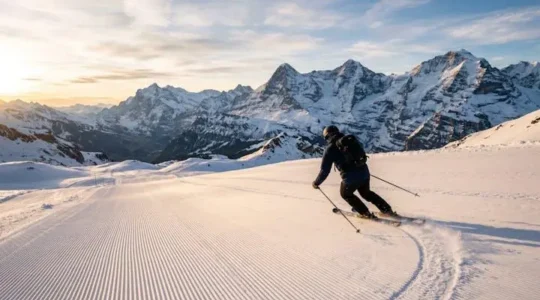 Skier carving clean turns down a wide groomed piste at sunrise, leaving thin arced tracks in the corduroy snow