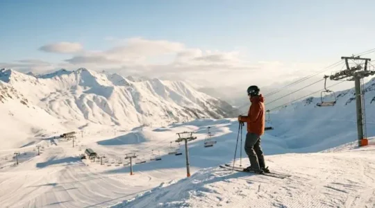 Skier standing at a mountain overlook studying the converging lift lines and terrain pods below
