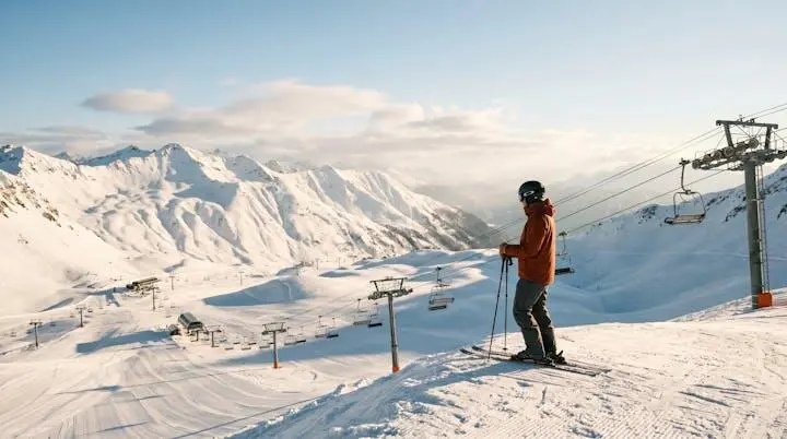 Skier standing at a mountain overlook studying the converging lift lines and terrain pods below