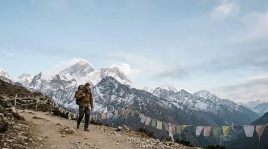 A lone trekker walking a wide Himalayan trail with prayer flags and snow-capped peaks in the distance, symbolizing the achievable journey to Everest Base Camp
